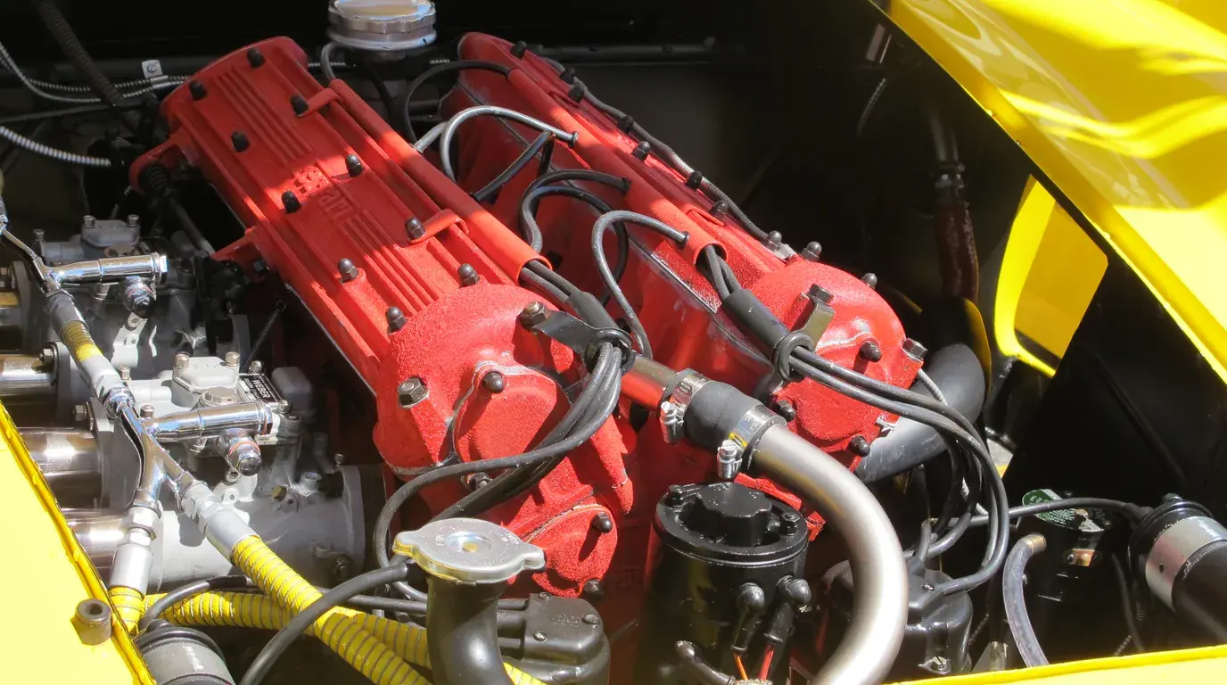 A Ferrari Lampredi four-cylinder engine with red cam covers, seen in an open yellow engine bay.